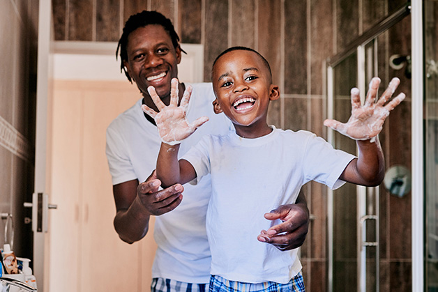 Father & son playfully washing their hands together in the bathroom smiling