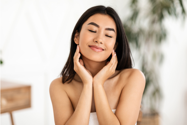 A smiling young woman with dark hair, closed eyes, and her hands framing her face.